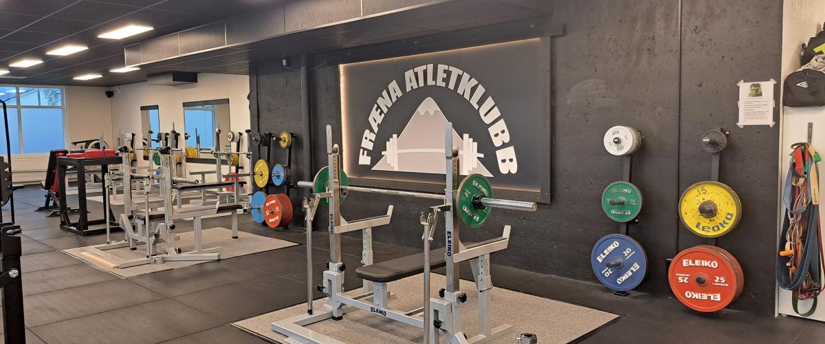 To benkpresstativ med svart vegg bak. På den svarte veggen henger et stort banner/plakat med logoen til Fræna Atletklubb.