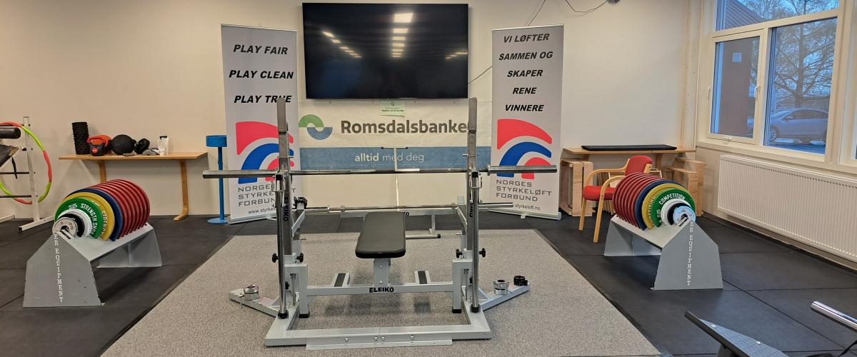 I det ene hjørnet av anlegget har de lagt opp til konkurranse. Her står det plassert et benkpresstativ med stativer til vektskiver på begge sider. Bak henger et sponsorbanner for romsdalsbanken og to roll-ups med logo og slagordene til Norges Styrkeløftforbund. I tillegg er det satt opp en TV-skjerm for dommersignaler. 