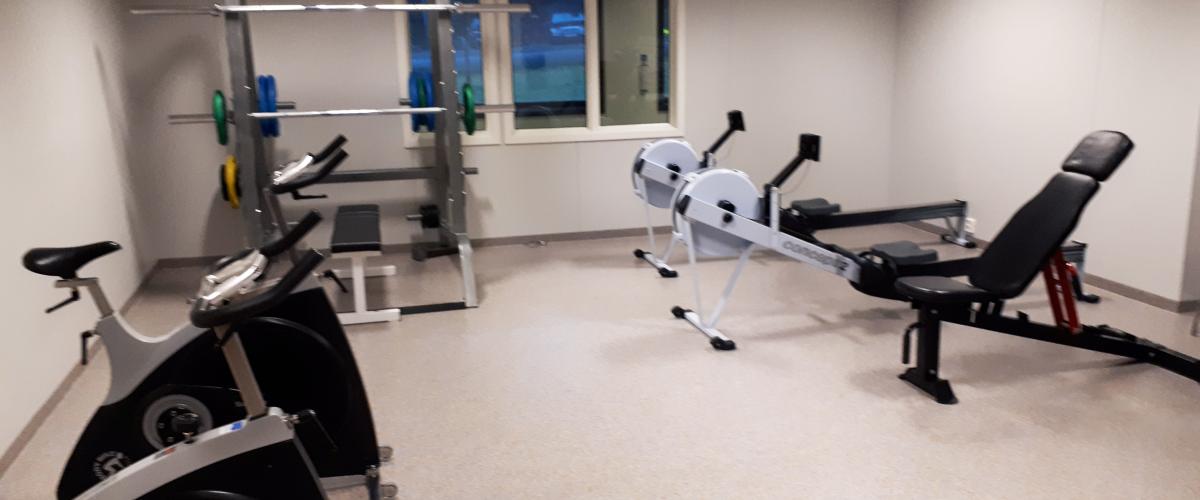 Styrketreningsrom. Foto: Gode idrettsanlegg Styrketreningsrom med 2 sykler, 2 romaskiner, 1 skråbenk, 1 stativ for trening med frivekter