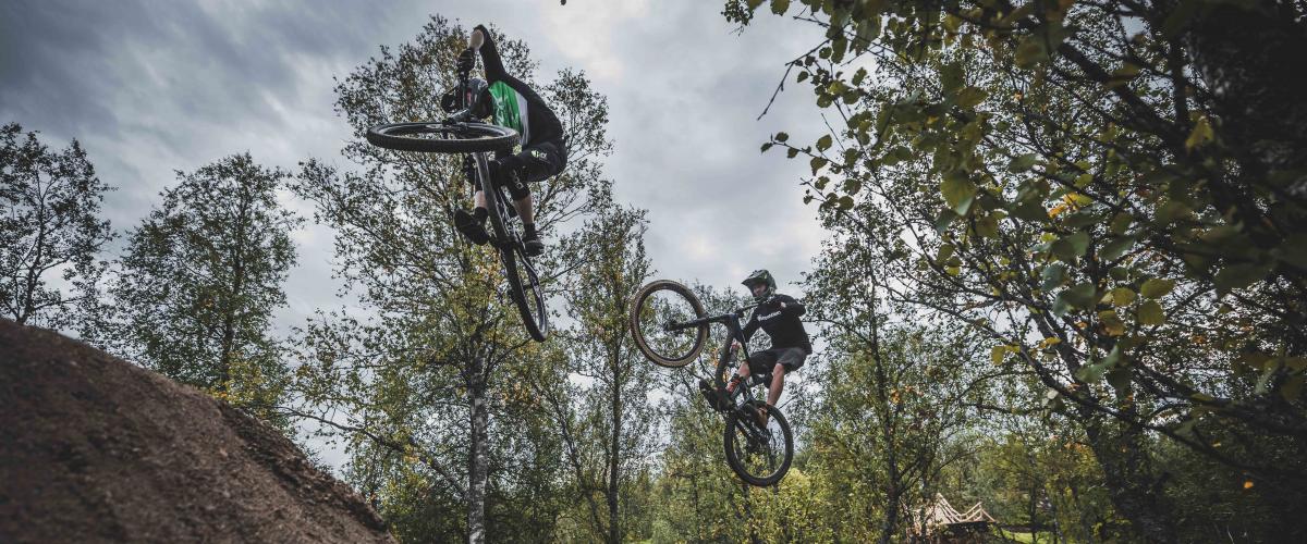 To terrengsyklister på vei over et hopp.