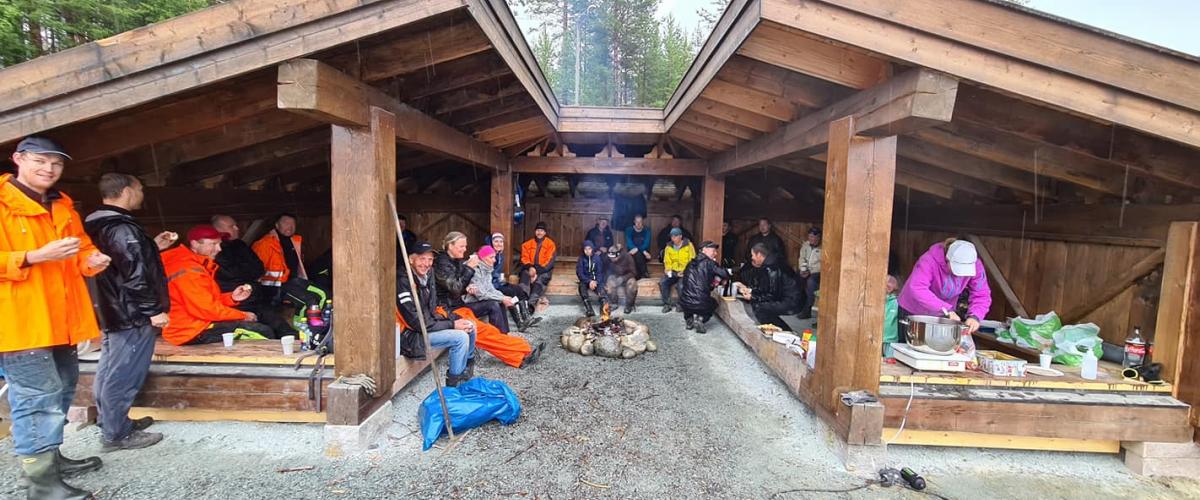 Dugnadsgjengen sitter i gapahuk og har det hyggelig mens det grilles.