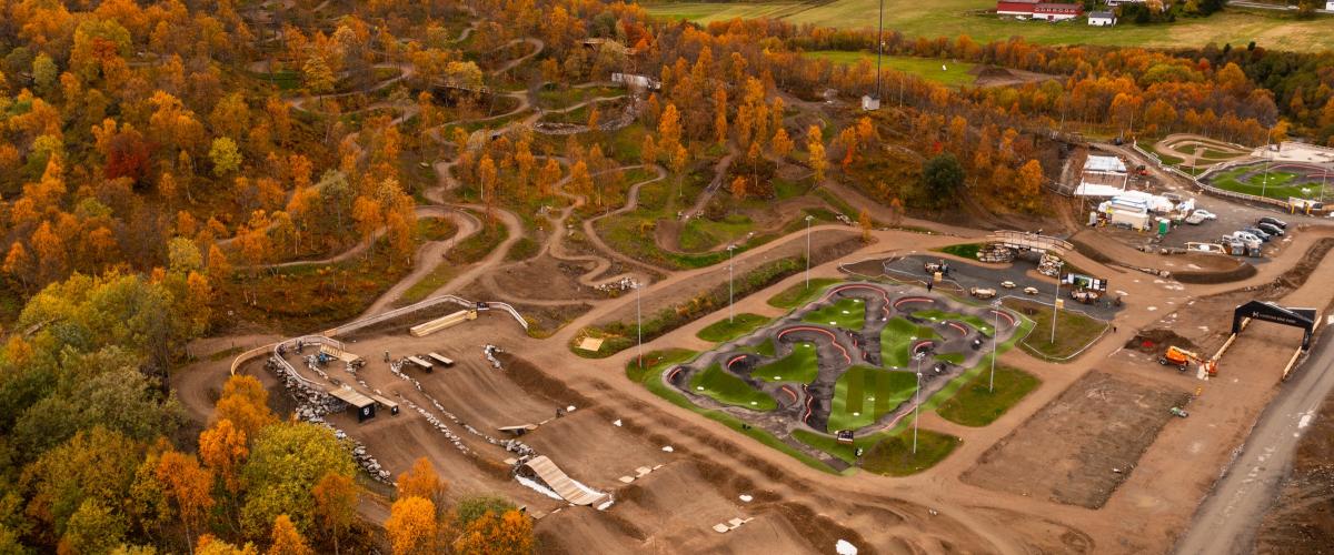 Sykkelpark i forgrunnen med terrengsykkelløyper som snor seg oppover en lang bakke i bakgrunnen.