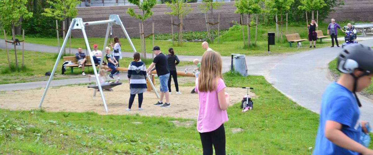 Huskestativ i parken, mange barn og voksne i parken.