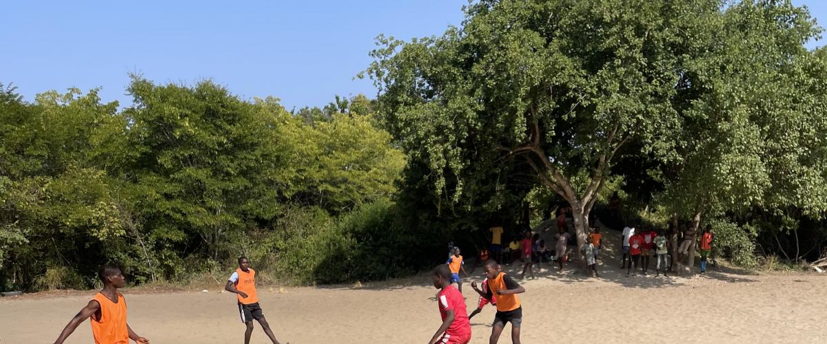 Noen barn spiller fotball på en bane av sand