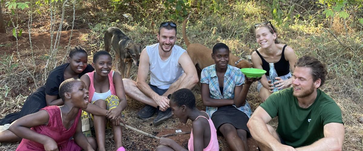 Den norske delegasjonen sitter på bakken med noen lokale jenter. 