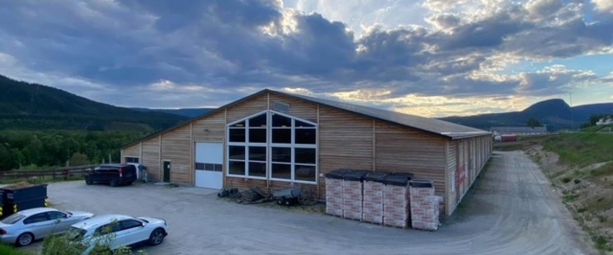 Ridehallen utenfra, lagringsplass på kortsida som ikke er mot innkjøring. Stort glassvindu midt på veggen for godt utsyn fra innendørs ridebane.