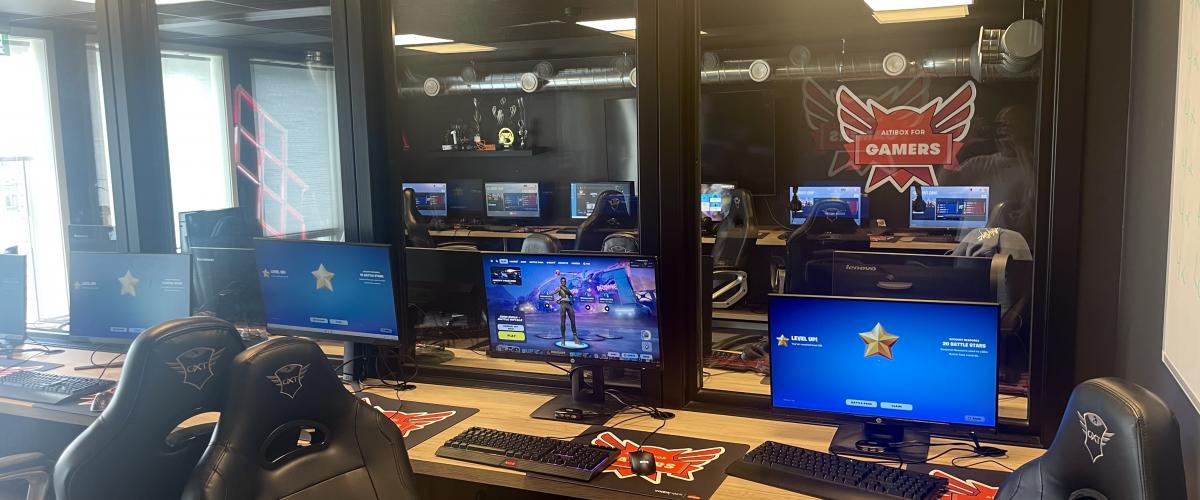 Klubbhuset har to gamingrom utstyrt med mange gamingplasser og er det første idrettslaget som tilbyr organisert e-sport. Foto: Gode idrettsanlegg bilde av gamingplasser med pc og soler, med vindu inn til det andre spillromet