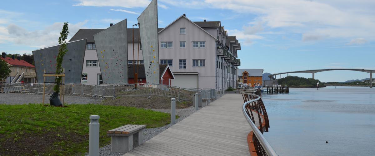 Strandpromenaden med belysning, tredekke og gjerde går mellom parken og sundet.