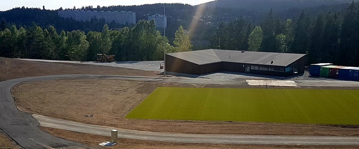 Kustgressbane med rulleskiløype rundt og et klubbhus bak.
