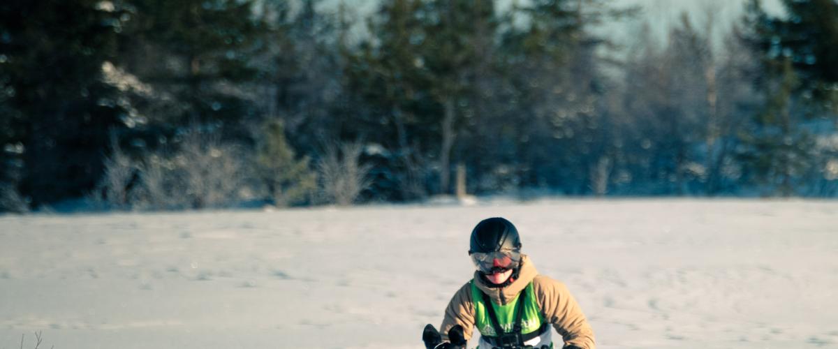 Anlegget er universelt utformet og løypenettet er tilgjengelig for både pulk, sparkesykkel, vognkasser, sykkel, løping og snørekjøring. Foto: Yannic A. Schuster Bilde av hundefører i sittepulk med fire hunder som trekker.