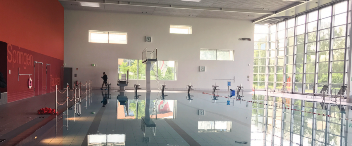 Innside av svømmehall med basseng og hoppetårn. 