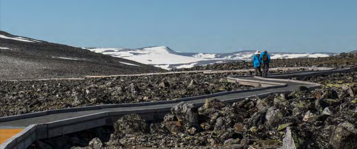 Bilde av to gående på en gangbane ved foten av Galdhøpiggen. Foto: Skjermdump fra KS sin veileder om "Vill natur for alle"