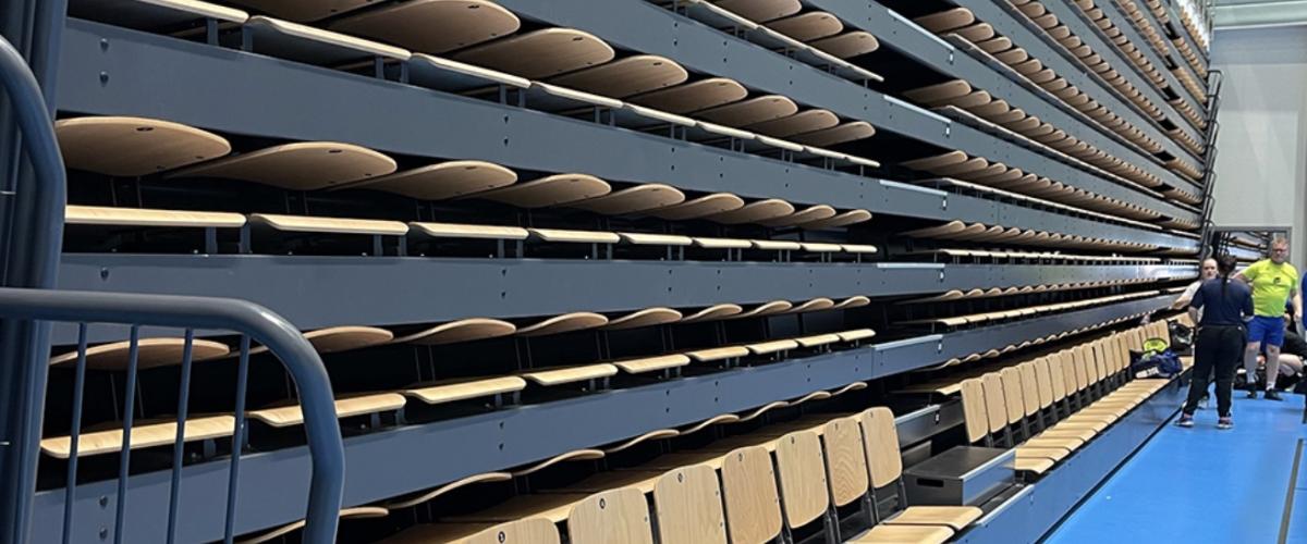 Bildet viser tribuneseter i en hall på Åsane Arena, stablet i flere rader og klar for tilskuere.