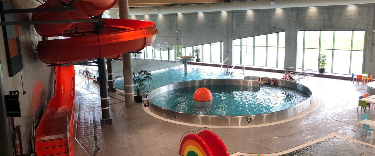 Barnebasseng med liten sklie i forgrunnen. Aktivitetsbasseng bak. Til venstre en stor sklie.