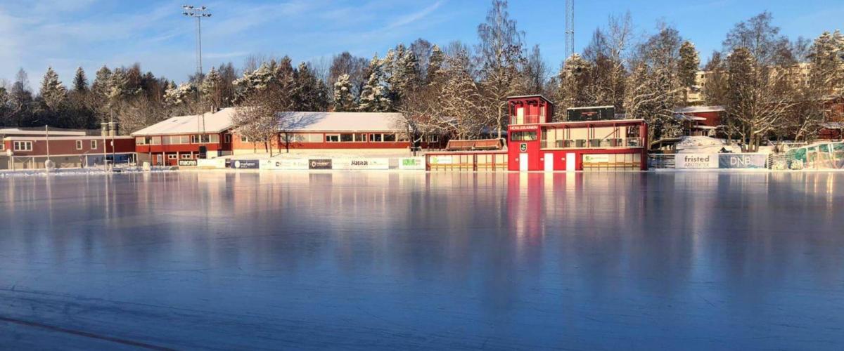 Bilde av hoslebanen en fin solskinnsdag vinterstid. I forgrunnen ligger isen, mens man i bakgrunnen ser klubbhuset.