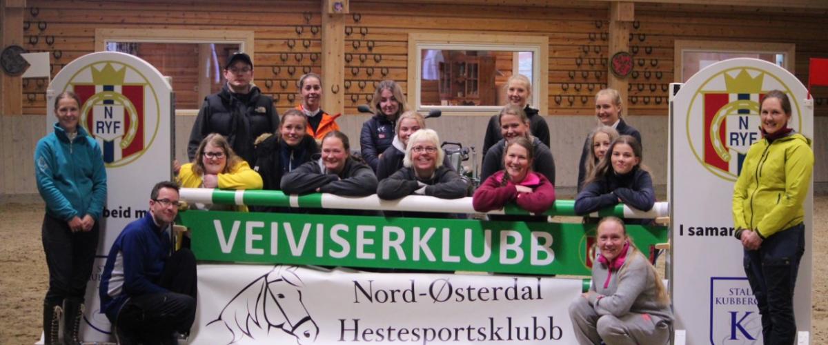 Hestesportsklubben i ridehus foran plakat som det står veiviserklubb på