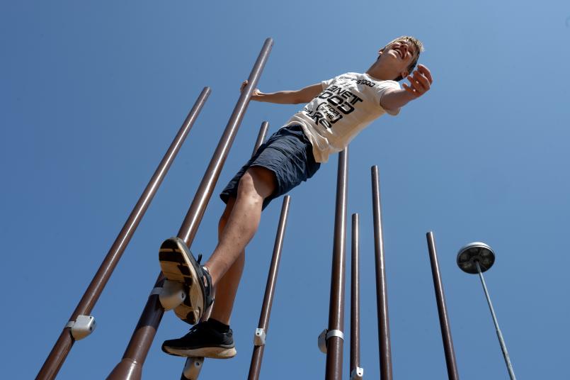 Gutt som klatrer i klatrestativ laget av lyktestolper. 