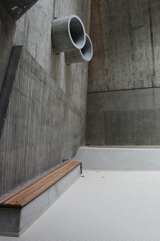 Betongvegg med ventilasjonsrør og benk med tilluft bak. 