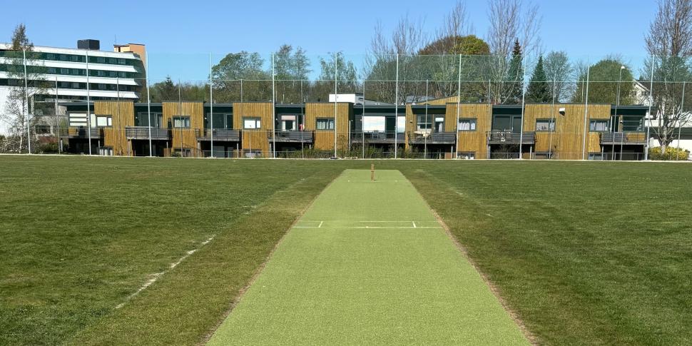 Bilde viser cricketbanen av kunstdekke som ligger midt på en gressbane, med bygninger og nettgjerde i bakgrunnen.